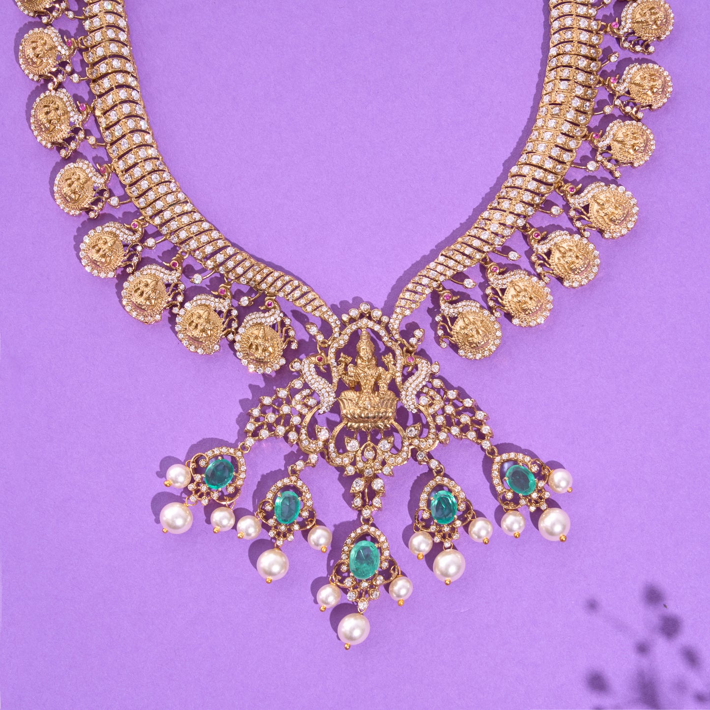 Ornate gold necklace with emeralds and pearls on a purple background